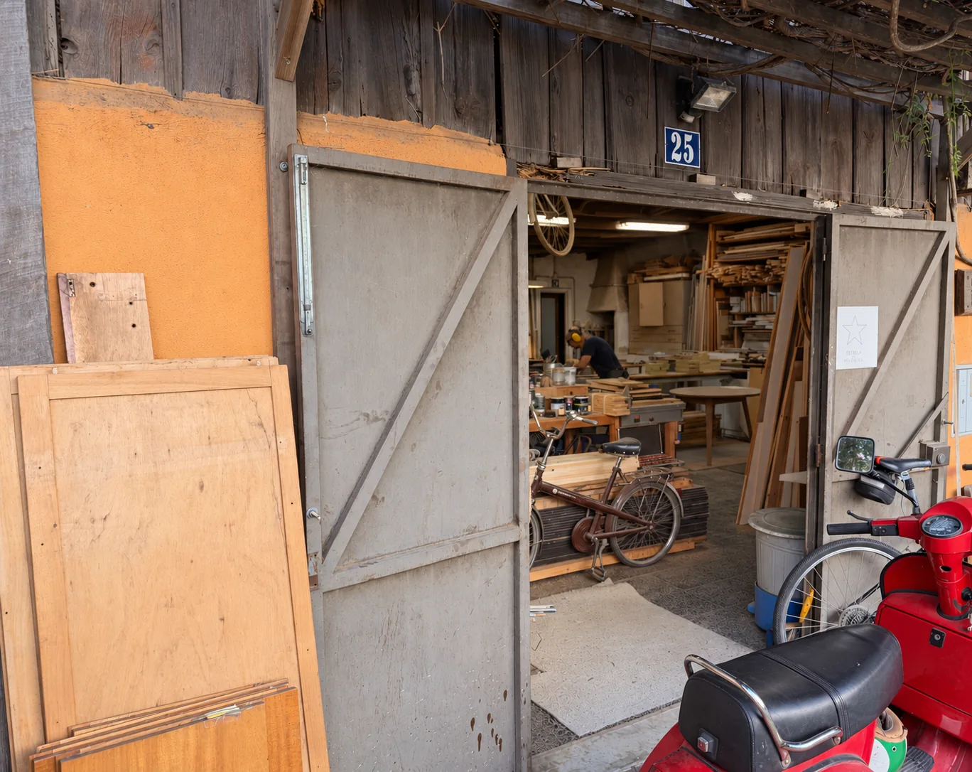 Open wooden workshop doors with timber, workbenches and a bicycle inside.